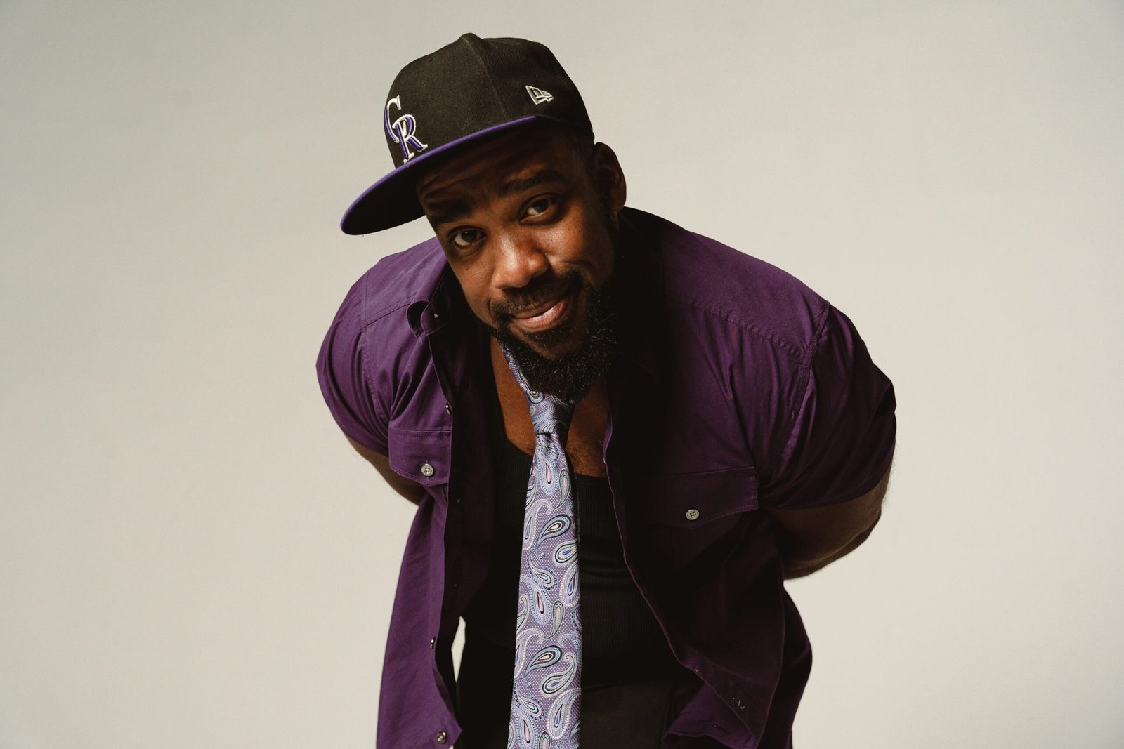Bad Juju, Denver stand-up comedian, in a purple shirt and Rockies cap